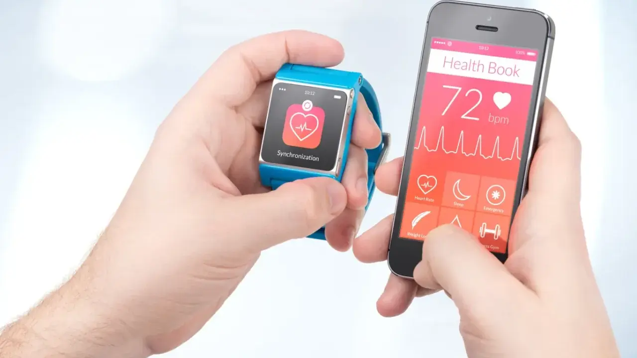 Dwie ręce trzymają smartfon i smartwatch. Na ekranie telefonu widnieje "Health Book" z pulsem 72 bpm. Puls 65 co oznacza? To dobry wynik, świadczący o dobrej kondycji.