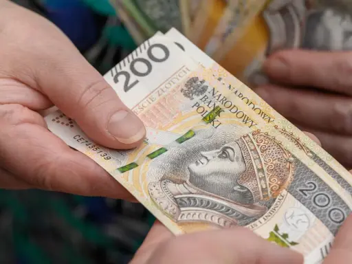 Dwie dłonie przekazują sobie banknot 200 zł. Czy opieka nad dzieckiem niepełnosprawnym wlicza się do emerytury?