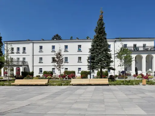Sanatorium Świt w Solcu-Zdroju, biały budynek z balkonami i łukami, otoczony zielenią i kwiatami.