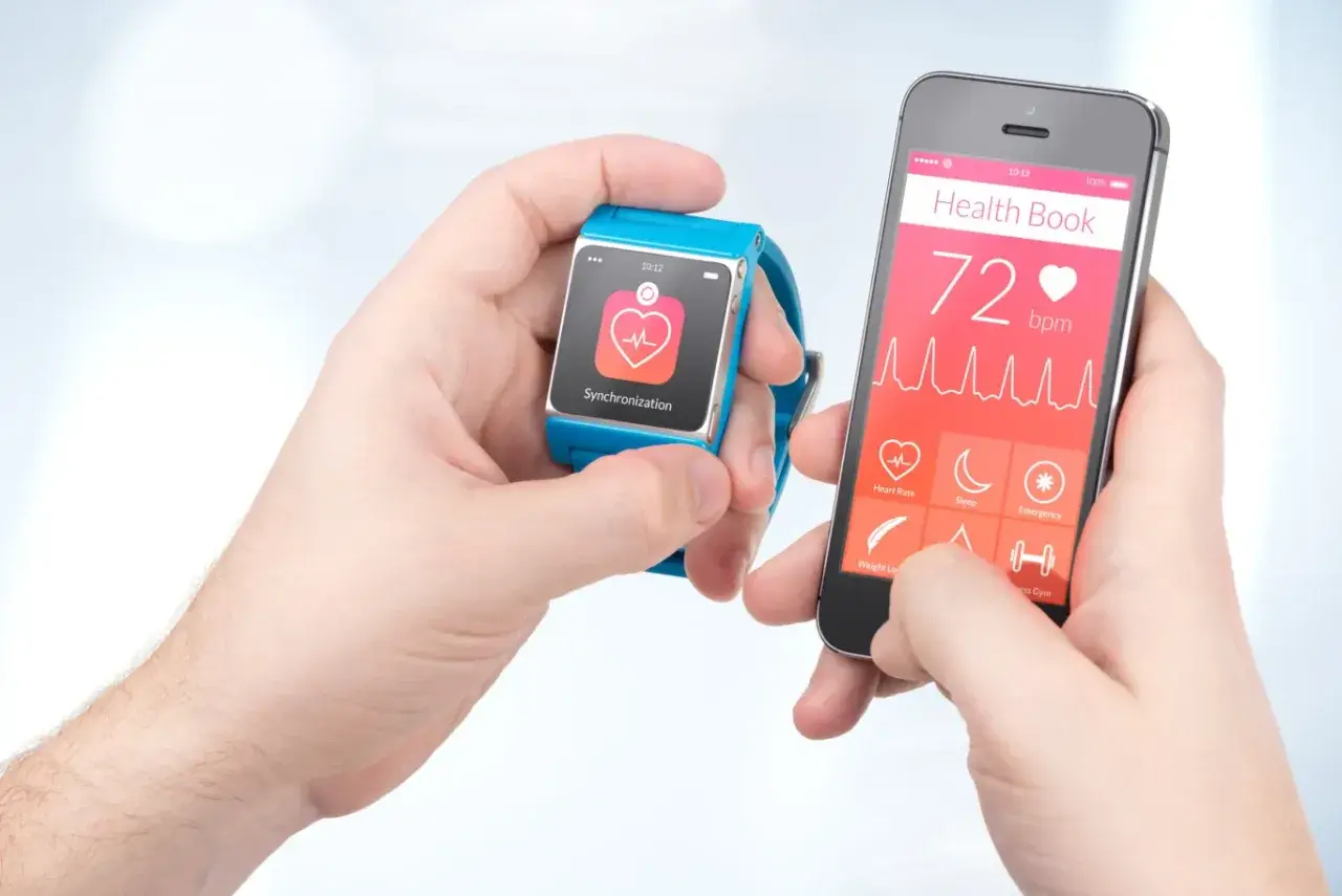 Dwie ręce trzymają smartfon i smartwatch. Na ekranie telefonu widnieje "Health Book" z pulsem 72 bpm. Puls 65 co oznacza? To dobry wynik, świadczący o dobrej kondycji.