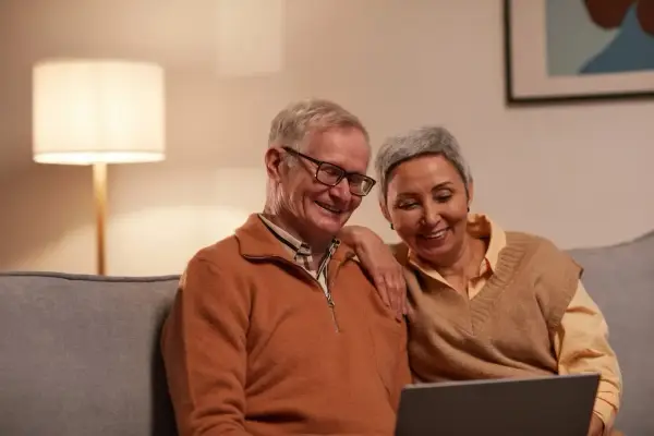 Uśmiechnięta para seniorów przegląda coś na laptopie, być może szukając informacji, czy chorobowe wlicza się do emerytury KRUS.